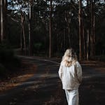 A woman strolls through a serene forest road in autumn, embracing solitude and nature.