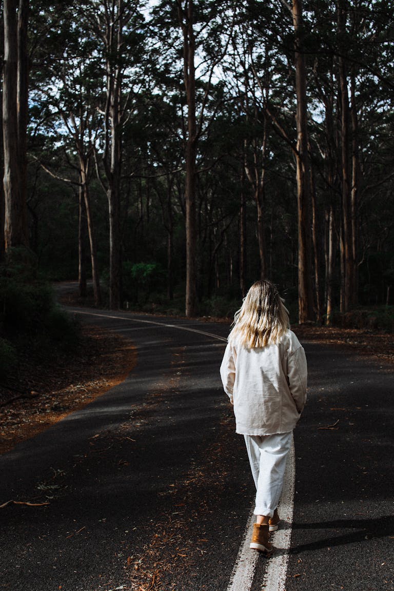 A woman strolls through a serene forest road in autumn, embracing solitude and nature.