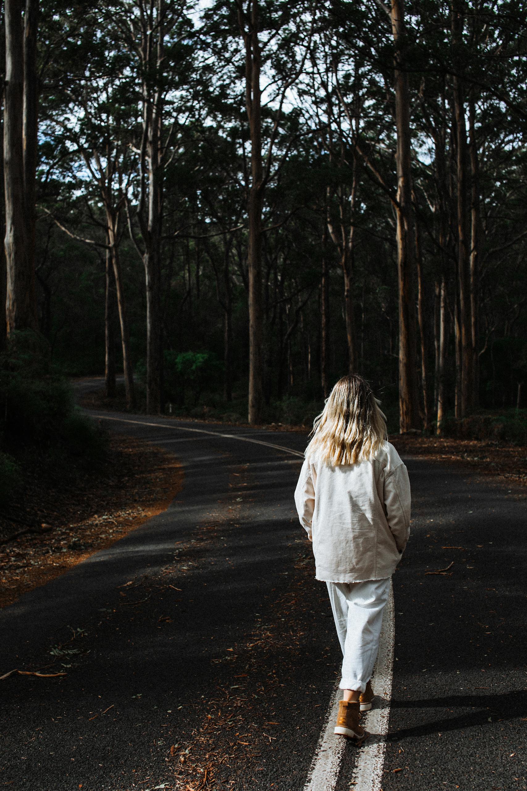 A woman strolls through a serene forest road in autumn, embracing solitude and nature.